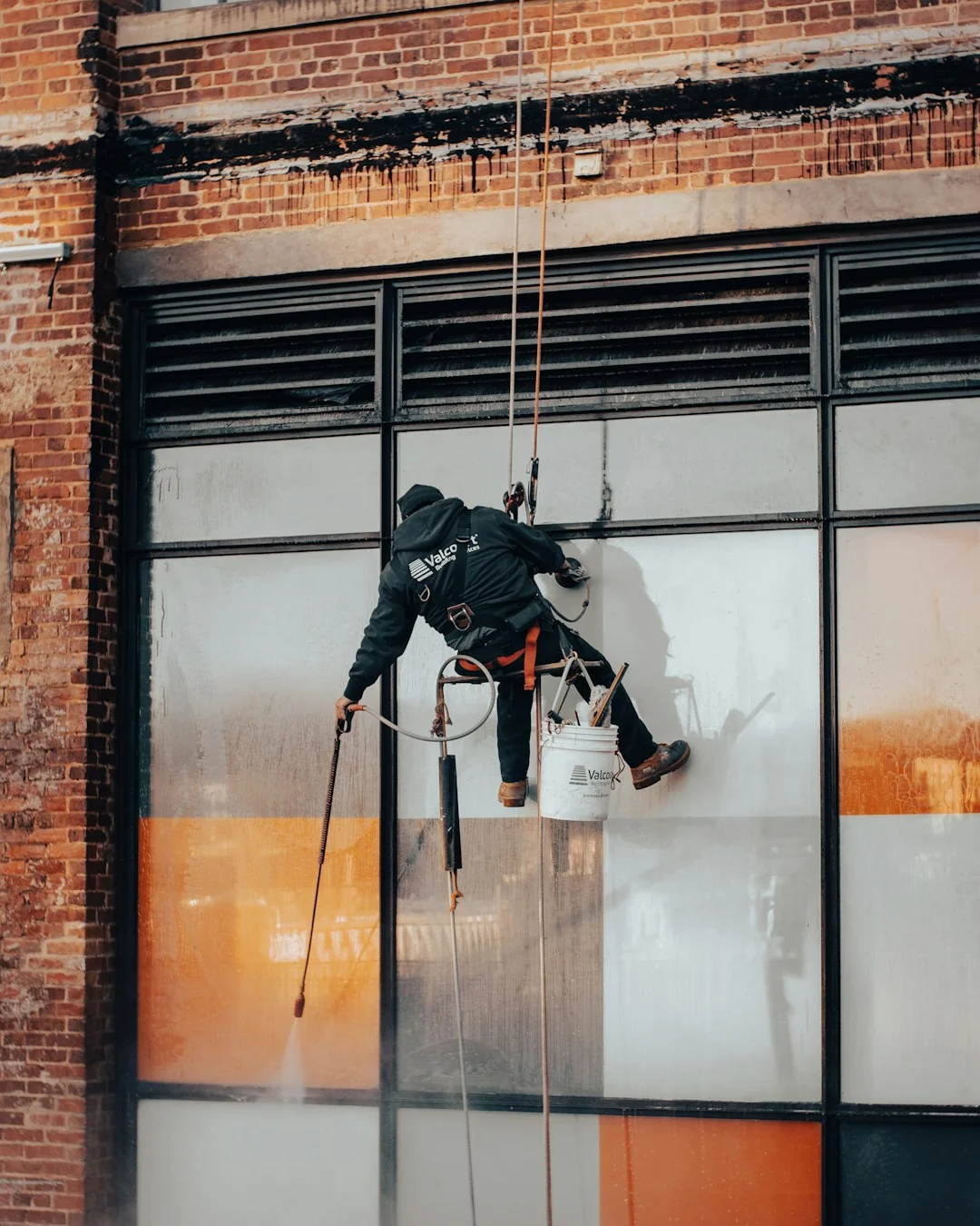 project-01-c Two workers are cleaning windows on a modern glass building facade from a suspended platform.