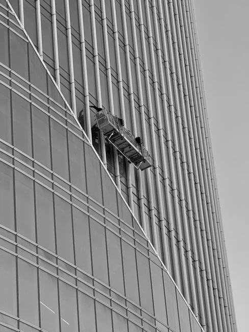 High-rise window washers in safety gear cleaning a skyscraper facade.